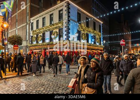 Festlicher Abend in Dublin, Temple Bar Pub mit beleuchtetem Kopfsteinpflaster, hektischer Menschenmenge und Weihnachtsdekoration. Stockfoto