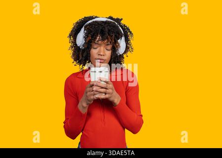 Junge Frau, die sich mit geschlossenen Augen entspannt, eine wiederverwendbare Tasse hält und Kopfhörer trägt Stockfoto