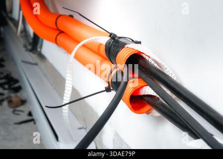 Innenkanal mit Glasfaserkabel. Oranges Rohr für Wandmontage mit Schnüren und losen Rohrkabeln. Kabelmanagement oder Kabelziehen in hoher Geschwindigkeit Stockfoto