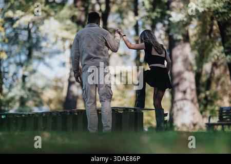 Zwei Personen in einem Park teilen sich einen verspielten Moment, halten Hände und tanzen an einem sonnigen Tag Stockfoto
