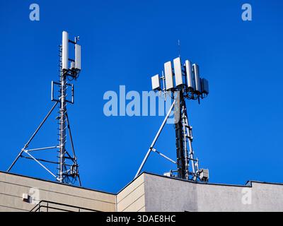 Telekommunikationsantennen und Mobilfunktürme auf dem Dach des Gebäudes vor blauem Himmel Stockfoto