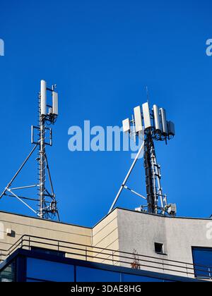 Telekommunikationsantennen und Mobilfunktürme auf dem Dach des Gebäudes vor blauem Himmel Stockfoto