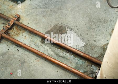 Wasserleckage im Boden oder im Untergeschoss des Kesselraums Schließen Sie eine Wasserpfütze unter Kupferrohren von Warmwassertanks und Betonboden. Sanitär-Notdienst Stockfoto
