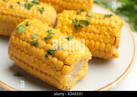 Stücke gekochter Maiskolben mit Petersilie auf weißem Tisch, Großaufnahme Stockfoto