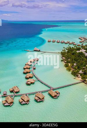 Hochwinkelblick auf ein Luxusresort mit Bungalows über dem Wasser in Taha'a, Französisch-Polynesien, zeigt den Kontrast zwischen dem tiefen Meer und der klaren Lagune. Stockfoto