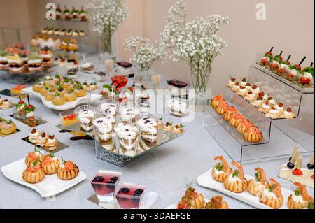 Ein üppiges Buffet mit einer Auswahl an Garnelenvorspeisen und Desserts auf mehrstufigen Ständen. Eine Fülle an exquisiten Kanapees und individuellen Desserts o Stockfoto