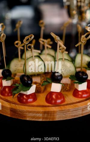 Nahaufnahme frischer Canapes mit Feta-Oliven und Kirschtomaten auf einem hölzernen Servierbrett. Festliche Gemüsekanapees auf einer Holzplatte mit Bambusskar Stockfoto