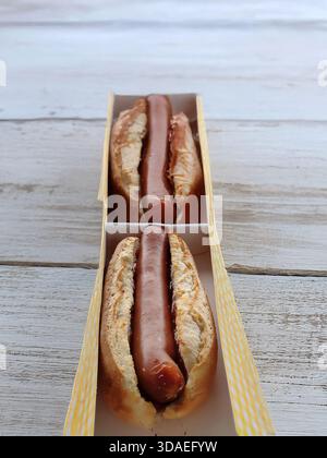 Eine vertikale Hochwinkelansicht von zwei köstlichen Hot Dogs, serviert in einem langen gelben und weißen Papiertablett. Die Würstchen sind in rustikales Brot eingebettet Stockfoto