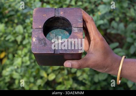 Nahaufnahme einer weiblichen Hand mit einem quadratischen, dunkel gebeizten, alten Holzaschenbecher mit minimalistischem Blockdesign und einem zentralen kreisförmigen Aschensammler. Stockfoto