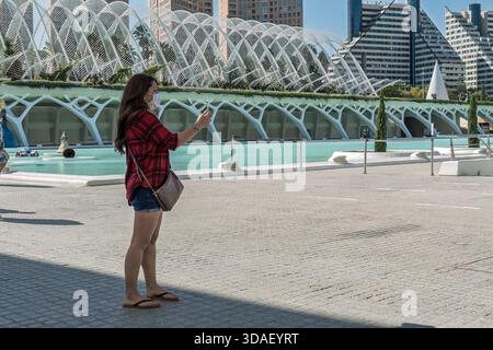 Frau mit Gesichtsmaske stehend und fotografiert mit ihrem Handy in der Stadt der Künste und Wissenschaften in Valencia, Spanien, Europa. Stockfoto