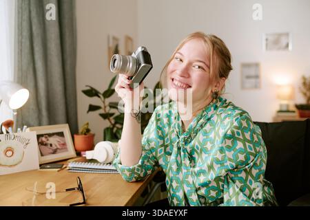 Porträt einer jungen Frau, die lächelt, während sie die Digitalkamera in Innenräumen hält Stockfoto