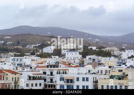 Aus der Vogelperspektive auf weiß getünchte Gebäude unter einem bewölkten Himmel, der Glockenturm der Evangelistria-Kirche, der durch die Szene hindurchdringt, Tinos, Tinos, GRE Stockfoto