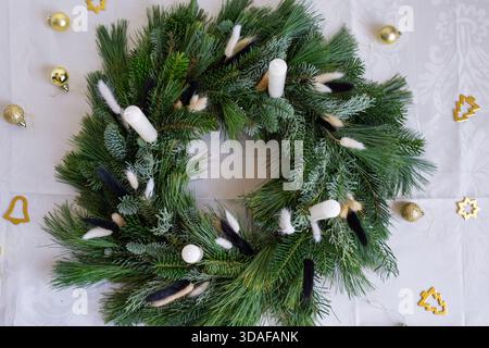Blick von oben auf einen üppig grünen Adventskranz aus Fichten- und Kiefernzweigen mit vier weißen Säulenkerzen. Stockfoto