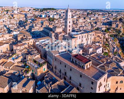 Aus der Vogelperspektive auf das sonnengeküsste, alte Sassi-Viertel mit seinen gestapelten Steinhäusern und dem hohen Dom mit langen Schatten, Matera, Basilicata Stockfoto