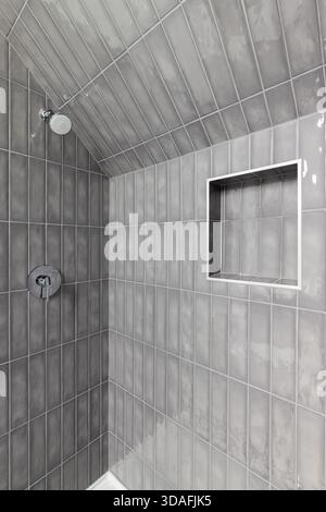 Eine moderne, grau geflieste Duschkabine mit eingebauter Nische für Stauraum und verchromtem Duschkopf. Stockfoto