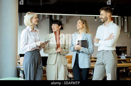 Vier Fachleute führen in einem modernen Büro mit Tageslicht und stilvollen Möbeln eine lebhafte Diskussion. Stockfoto