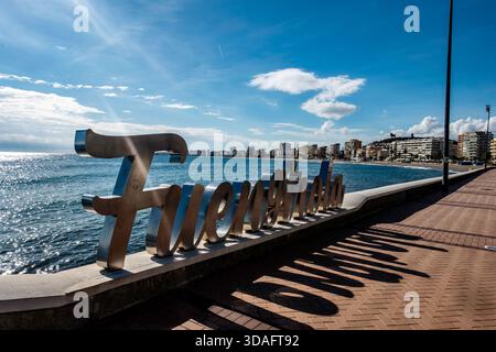 Großes silbernes 'Fuengirola'-Schild an der Strandpromenade. Fuengirola, Spanien, Mittelmeer, Hochhäuser in der Ferne. Sonniger Tag, langer Schatten Stockfoto