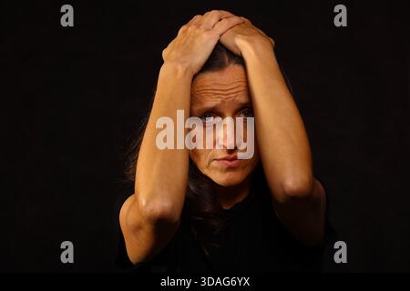 Eine beunruhigte Frau, die ihren Kopf mit beiden Händen hält. Starker Ausdruck von Depression, Angst, Angst und emotionalem Schmerz. Das Konzept des psychischen Gesundheitsproblems Stockfoto