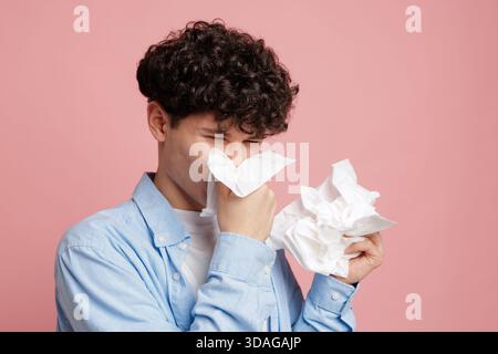 Junger Mann, der niesend und nasenbläst mit Geweben, die eine Erkältungsgrippeallergie zeigen, und Hygienekonzept im Atelier Stockfoto