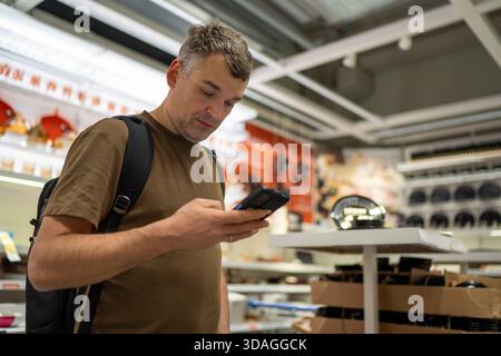 Mann, der im Geschäft einkaufen und Smartphone durchsucht Stockfoto