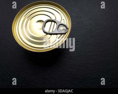 Eine Dose sitzt auf einer dunklen Oberfläche mit einem Schlüssel an der Oberseite und wartet darauf, geöffnet zu werden. Die Einstellung scheint tagsüber eine Küche zu sein. Stockfoto