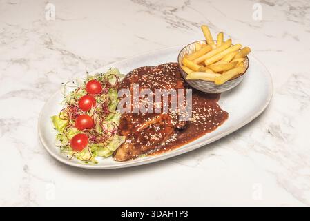 Gegrillte Baby-Back-Rippchen mit einer Gewürzcreme, die eine dunkle Kruste bildet, serviert mit Maisbrot und Dill-Gurken Stockfoto