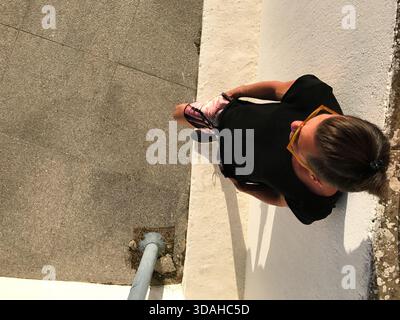 Blick von oben auf einen jungen Mann, der auf einer städtischen Straße steht, seinen Rücken gegen eine weiße Wand lehnt, während er auf die Straße blickt. Durch warmes Tageslicht Stockfoto