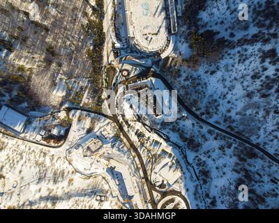 Von oben aus sehen Sie die Zufahrtsstraßen der Eisbahn Medeu, die geschwungenen Parkplätze und das umliegende schneebedeckte Gelände in einer Bergschlucht Stockfoto