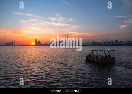 Skyline von Dubai bei Sonnenuntergang mit Booten im Fluss, 4K-Tapete mit Blick auf die Skyline bei Sonnenuntergang im Winter Stockfoto