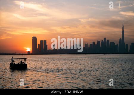 Skyline von Dubai bei Sonnenuntergang mit Booten im Fluss, 4K-Tapete mit Blick auf die Skyline bei Sonnenuntergang im Winter Stockfoto