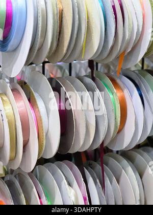 Fröhlicher und farbenfroher Stapel Satinbandspulen in Kurzwarenladen. Lebendiger Hintergrund der handwerklichen Vorräte für Dekoration und kreative Geschenkverpackungen Stockfoto