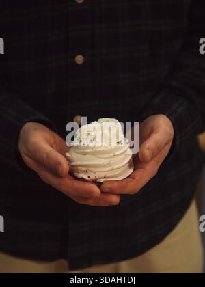Mann hält Meringue-Kuchen in warmem, schwachem Licht – vertikale Nahaufnahme Stockfoto