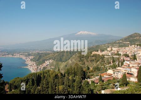 Panoramablick auf Taormina in Sizilien mit dem Ätna im Hintergrund und dem Mittelmeer, das von der Seite aus sichtbar ist und die Stadt und die Berge miteinander verbindet Stockfoto