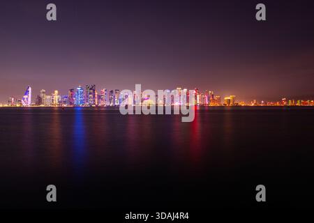 Doha, Katar: 20. März 2025. Lebhafte nächtliche Skyline der Doha Corniche über ruhigem Wasser mit farbenfrohen Lichtern der Stadt, die sich über die Hafenlandschaft reflektieren Stockfoto