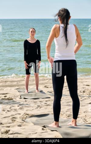 Yogalehrer für Erwachsene mit schwarzem Haar in schwarzem Outfit führt junge Frauen mit langen dunklen Haaren in weißem Oberteil und schwarzen Leggings. Szene auf S aufgenommen Stockfoto