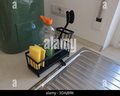 Schwarzer Ständer mit Reinigungsmittel, Bürste und Schwamm in der Küche in der Nähe des Waschbeckens. Sauberkeit im Haus. Pflege und Reinigung. Stockfoto