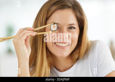 Frau, die Sushi mit Essstäbchen über das Auge hält Stockfoto