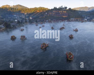 Ruhiger Blick aus der Luft auf schwimmende Häuser auf dem nebeligen See bei Sonnenaufgang. Ruhiges Wasser und goldenes Licht auf dem Bergdorf schaffen eine wunderschöne und friedliche Landschaft Stockfoto