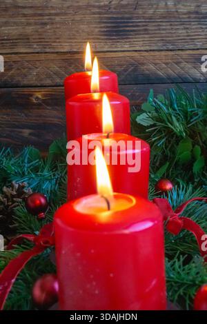 Eine hohe, eng angeordnete Reihe roter Kerzen brennt warm zwischen immergrünen Zweigen und festlichen Akzenten. Stockfoto