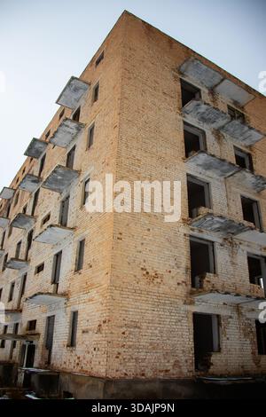 Flacher Blick auf die Ecke eines verfallenen Backsteingebäudes mit bröckelnden Balkonen in einer verlassenen Stadt Stockfoto