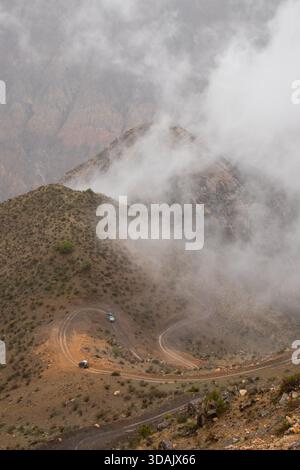 Blick von oben nach unten auf Autos, die in Haarnadelkurven auf einem felsigen, von Wolken bedeckten Berghang fahren Stockfoto