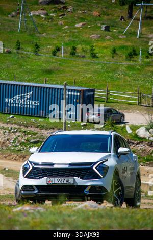 Naryn Region, Kirgisistan - 13. Mai 2024: Weißer Kia Sportage SUV fährt auf einer Feldstraße mit blauem Schiffscontainer und grünen Hügeln im Hinterland Stockfoto