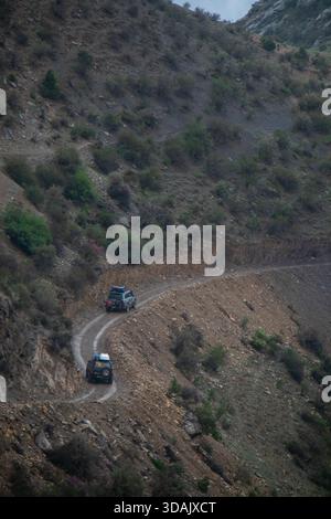 Naryn Region, Kirgisistan - 13. Mai 2024: Zwei Geländewagen fahren auf einem steilen Schotterpass durch enge Serpentinen Stockfoto