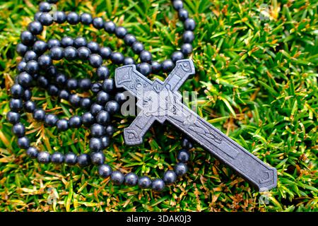 Dunkler Ebenholz-Rosenkranz mit aufwändig geschnitztem Kruzifix, das über blühendem gelbem Heidekraut auf üppig grünem Sträucher hängt und an friedliche christliche Hingabe erinnert Stockfoto