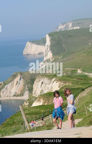 Besucher, die entlang des Küstenpfades mit Blick auf die Kreidefelsen der Seven Sisters, East Sussex, England, und an sonnigen Tagen die malerische Landschaft der South Downs erkunden Stockfoto