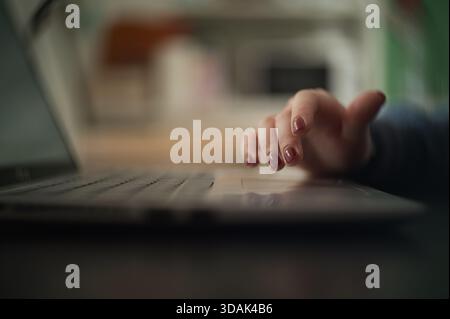 Nahaufnahme einer Hand mit polierten Nägeln, die sanft auf einer Laptop-Tastatur aufliegt. Der Vordergrund ist scharf, während der Hintergrund leicht verschwommen ist Stockfoto