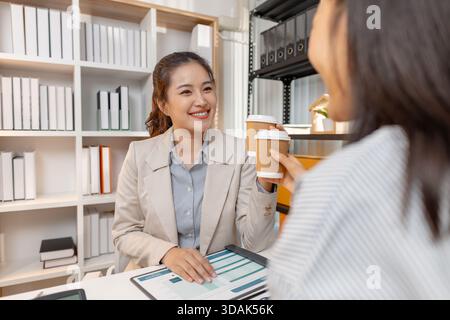 Zwei asiatische Geschäftsfrauen diskutieren gemeinsam in einem modernen Büro über Unternehmensstrategie und analysieren Finanzdokumente und Diagramme. Sie arbeiten zusammen und Stockfoto
