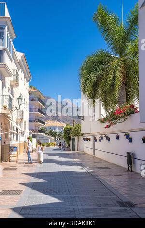 Nerja, Spanien - 9. September 2024: Ein Paar schlendert durch eine sonnige mediterrane Straße, gesäumt von weißen Gebäuden und Palmen. Stockfoto