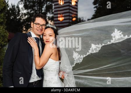 Interrassisches Paar feiert Hochzeitstag mit fließendem Schleier Stockfoto