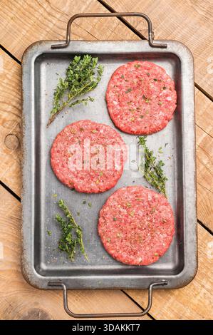 Rohe Hamburger Hackfleischpasteten für Burger mit Kräutern auf Tablett. Hölzerner Hintergrund. Draufsicht Stockfoto